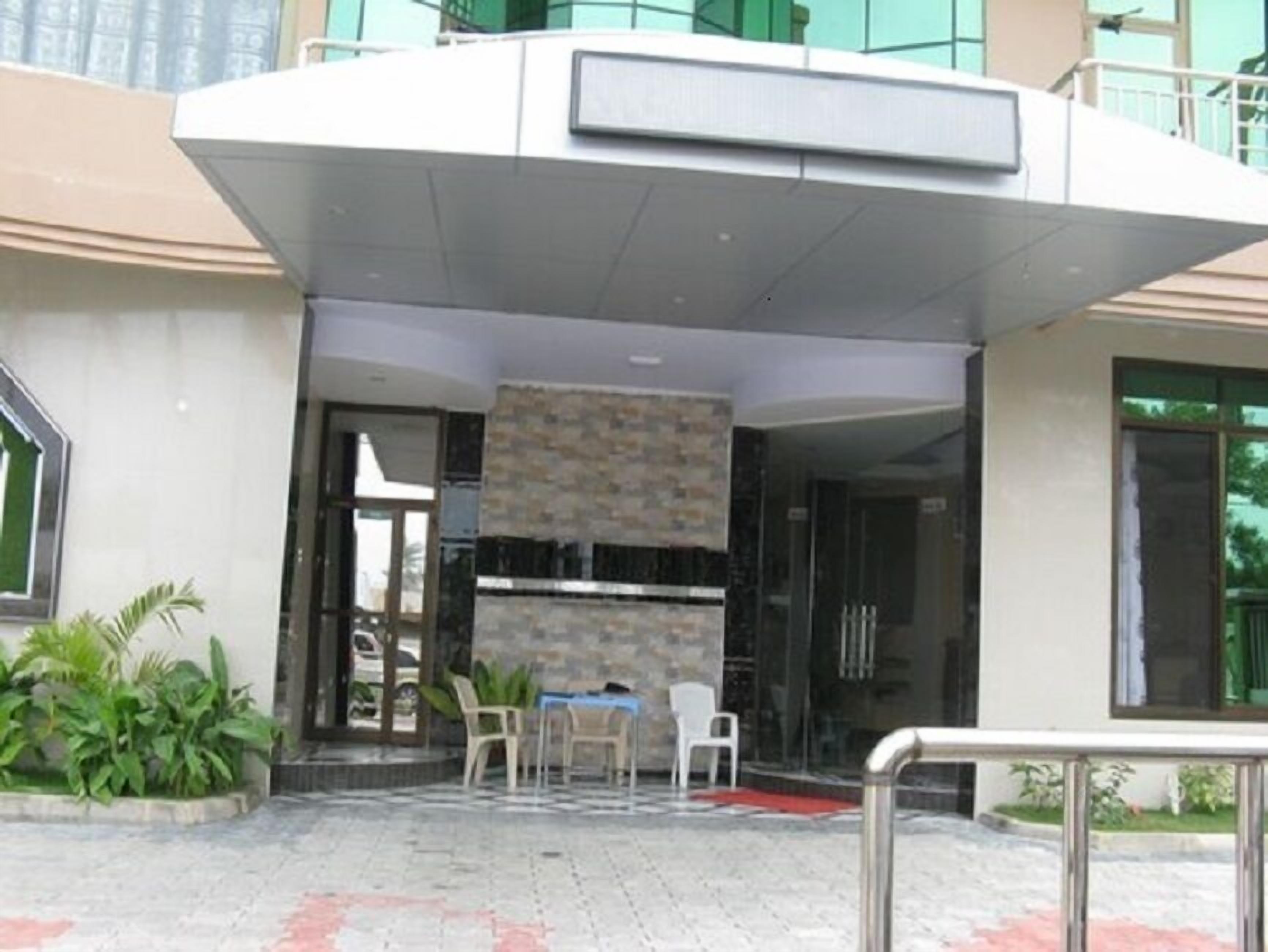 Una entrada moderna a un edificio con una zona de estar al aire libre techada, un muro de piedra y una puerta de cristal.