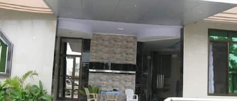 A modern building entrance with a covered outdoor seating area, a stone wall, and a glass door.