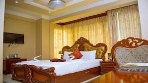 A hotel room with a large bed, a wooden headboard, a bedside table, and a TV mounted on the wall. - Rungwe Hotel (Dar es Salaam)