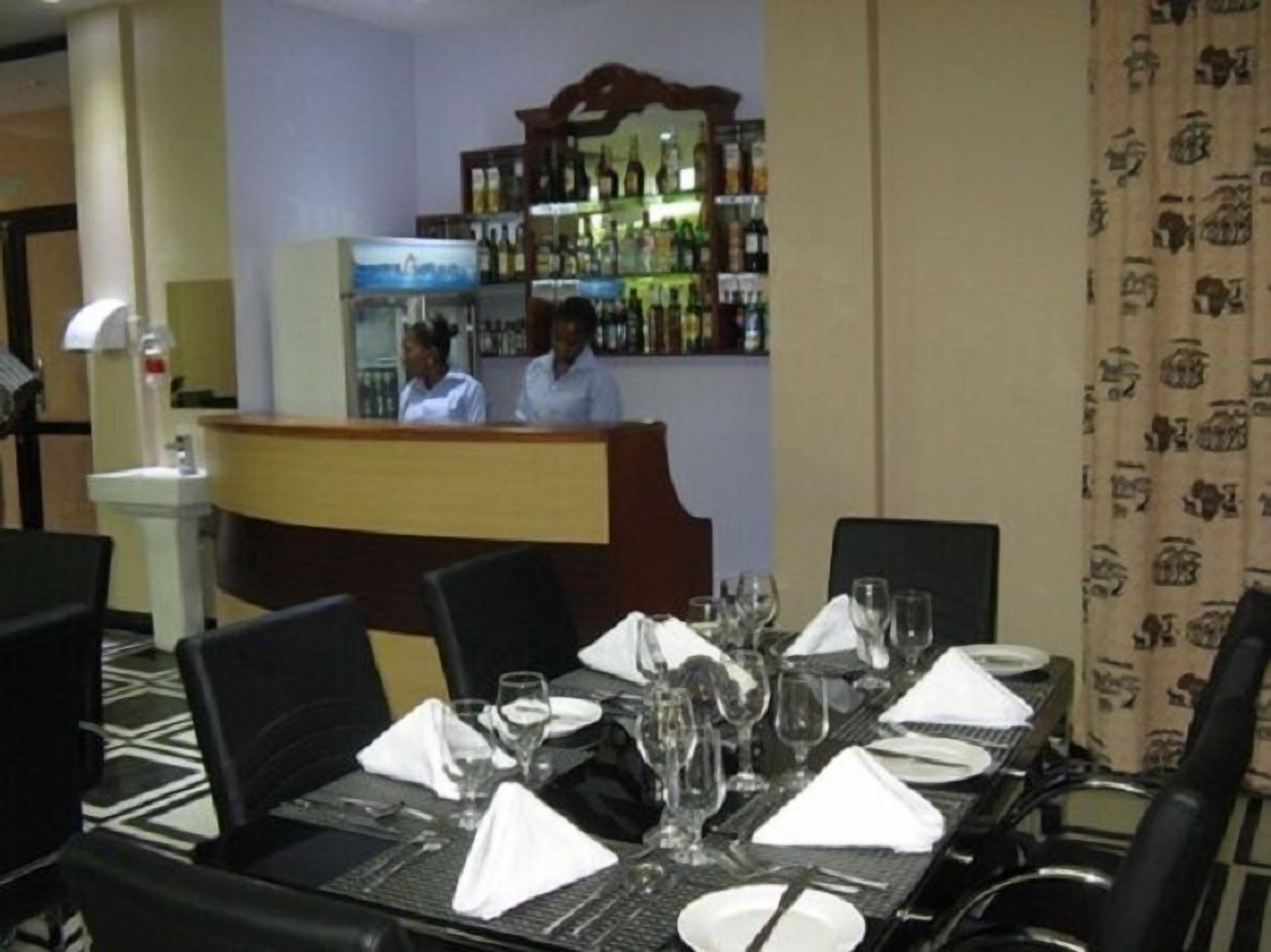 A restaurant with a bar area, neatly set tables with glasses and cutlery, and a patterned curtain.