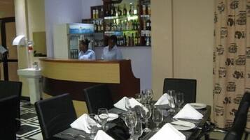 A restaurant with a bar area, neatly set tables with glasses and cutlery, and a patterned curtain.