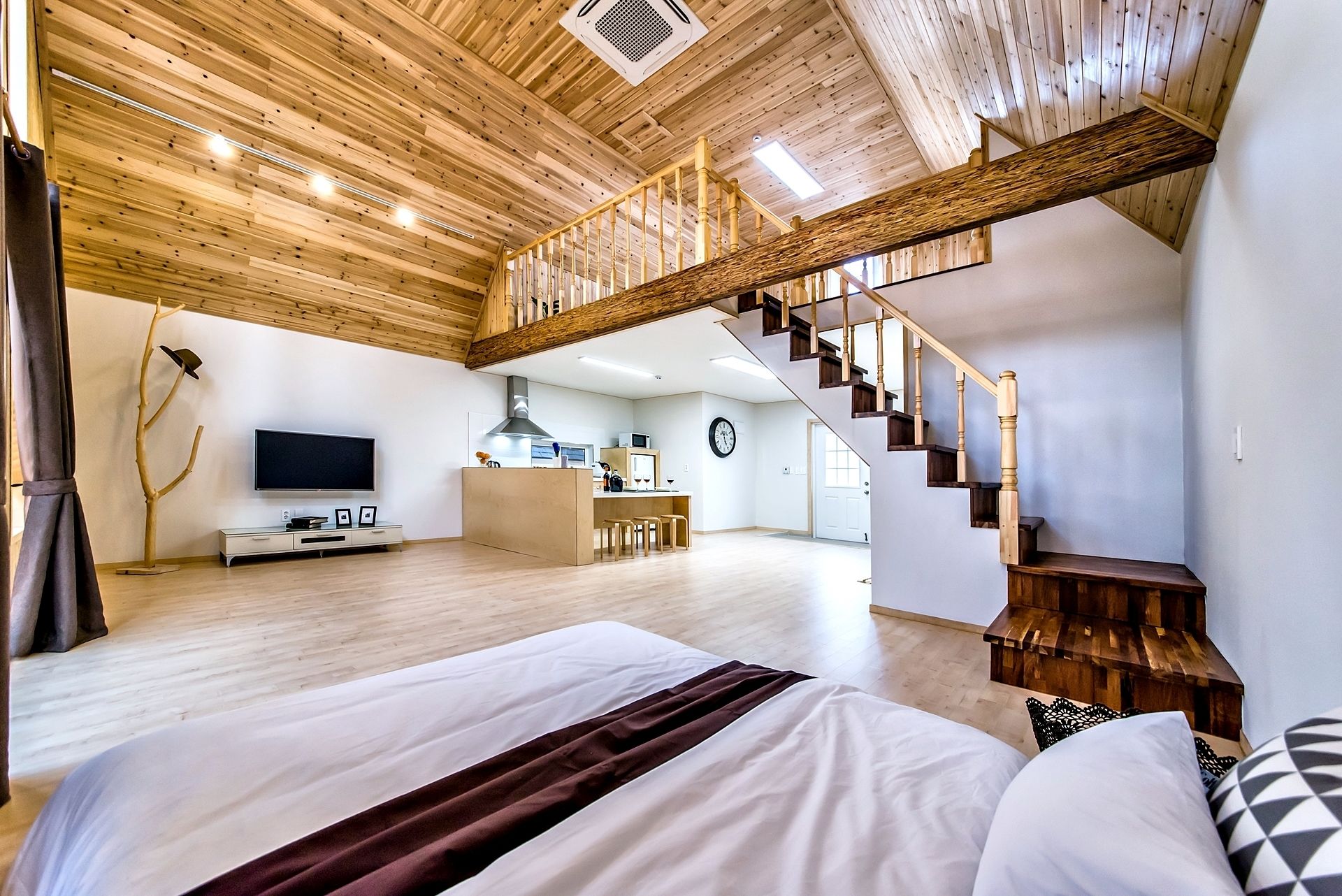 Une pièce spacieuse comprenant un grand lit, un escalier en bois, un coin cuisine et un espace de vie avec un téléviseur.