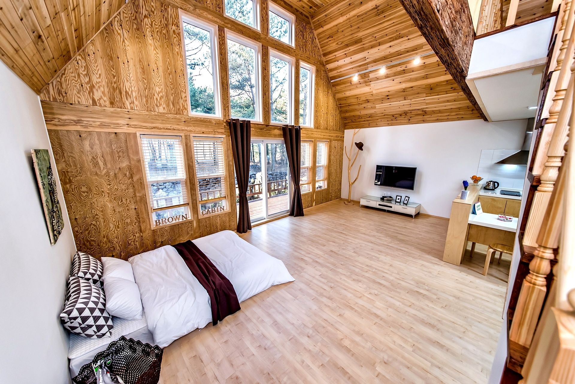 Een chalet met slaapkamer op entresol, grote ramen, een televisie en een kitchenette.