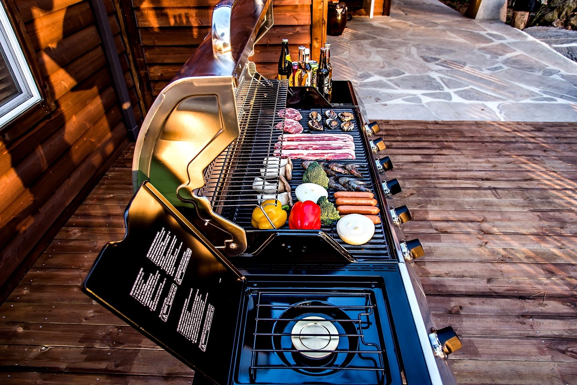 Una parrilla con diferentes carnes y verduras sobre una terraza de madera.
