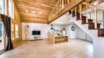A spacious living area with a wooden staircase, a kitchen island, and a television.
