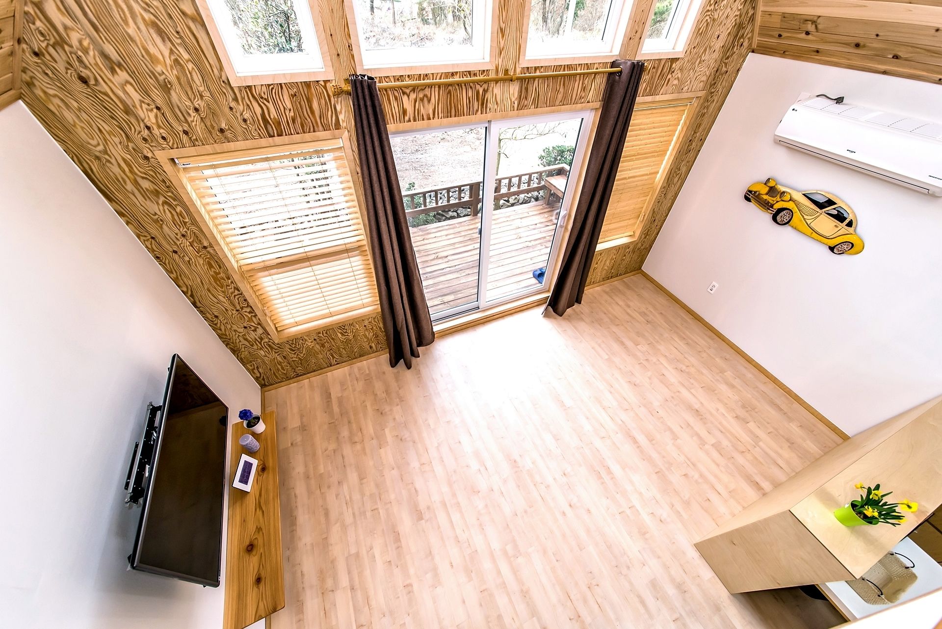 A room with a wooden ceiling, large windows, a sliding glass door, a flat-screen TV, and a toy car on the wall.