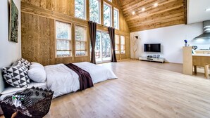 A spacious room with a high ceiling, wooden walls, and large windows. - Browncabin Pension (Jeju City)