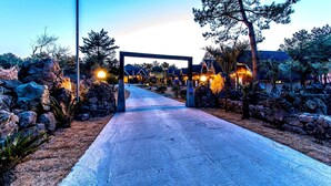 A pathway leading to a building with multiple rooms, surrounded by rocks and trees. - Browncabin Pension (Jeju City)