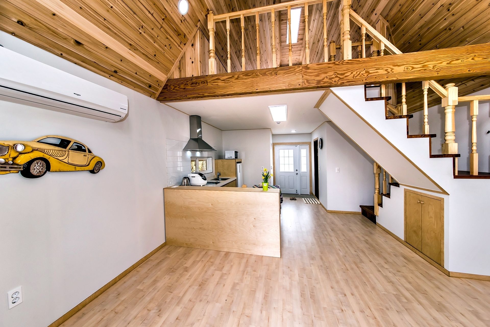 A spacious living area with a wooden ceiling, a kitchen with modern appliances, and a staircase leading to an upper level.