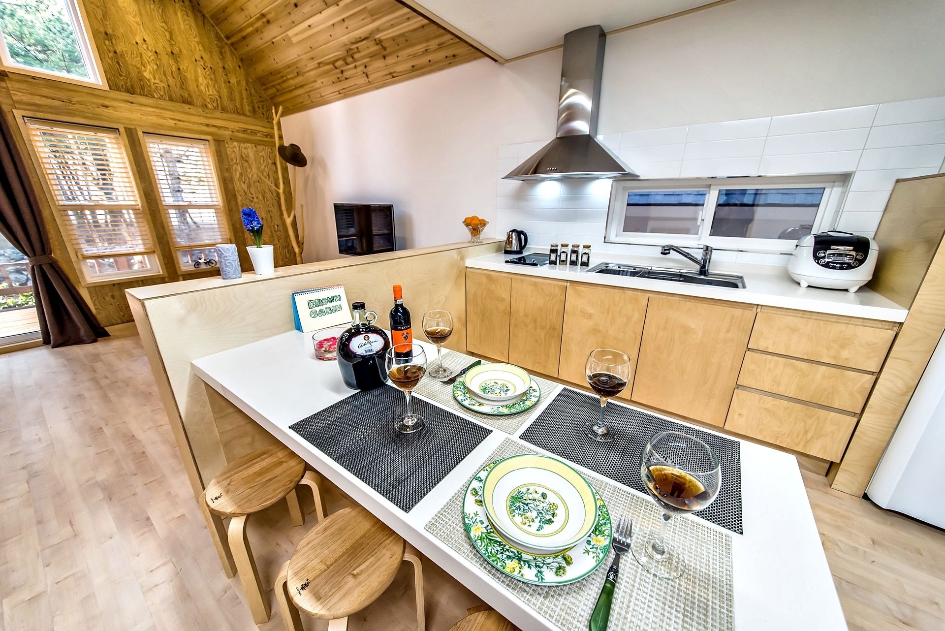 Una cocina moderna con armarios de madera, una campana extractora de acero inoxidable y una zona de comedor con una mesa dispuesta para dos.
