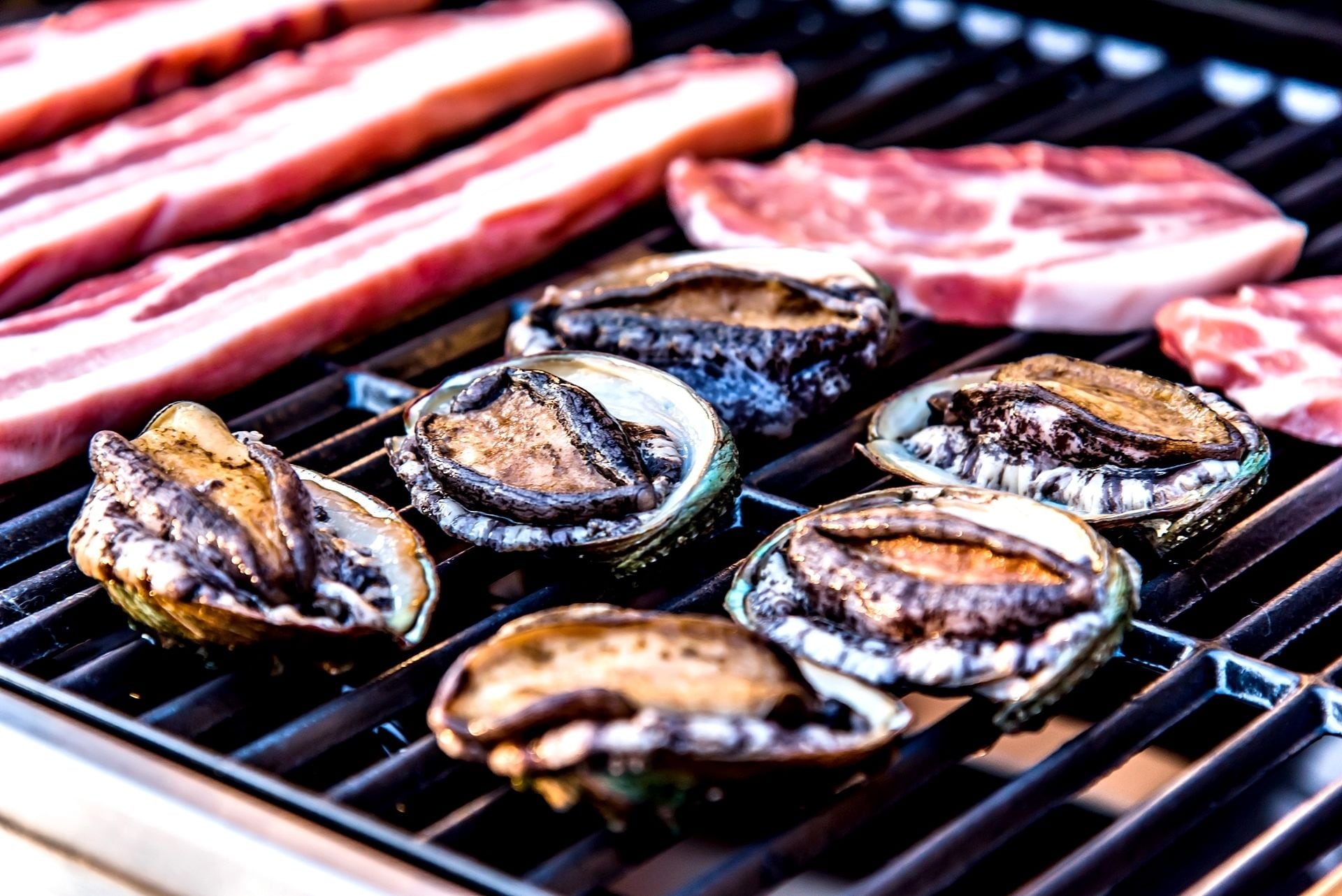 Des huîtres et des steaks grillent sur un barbecue.
