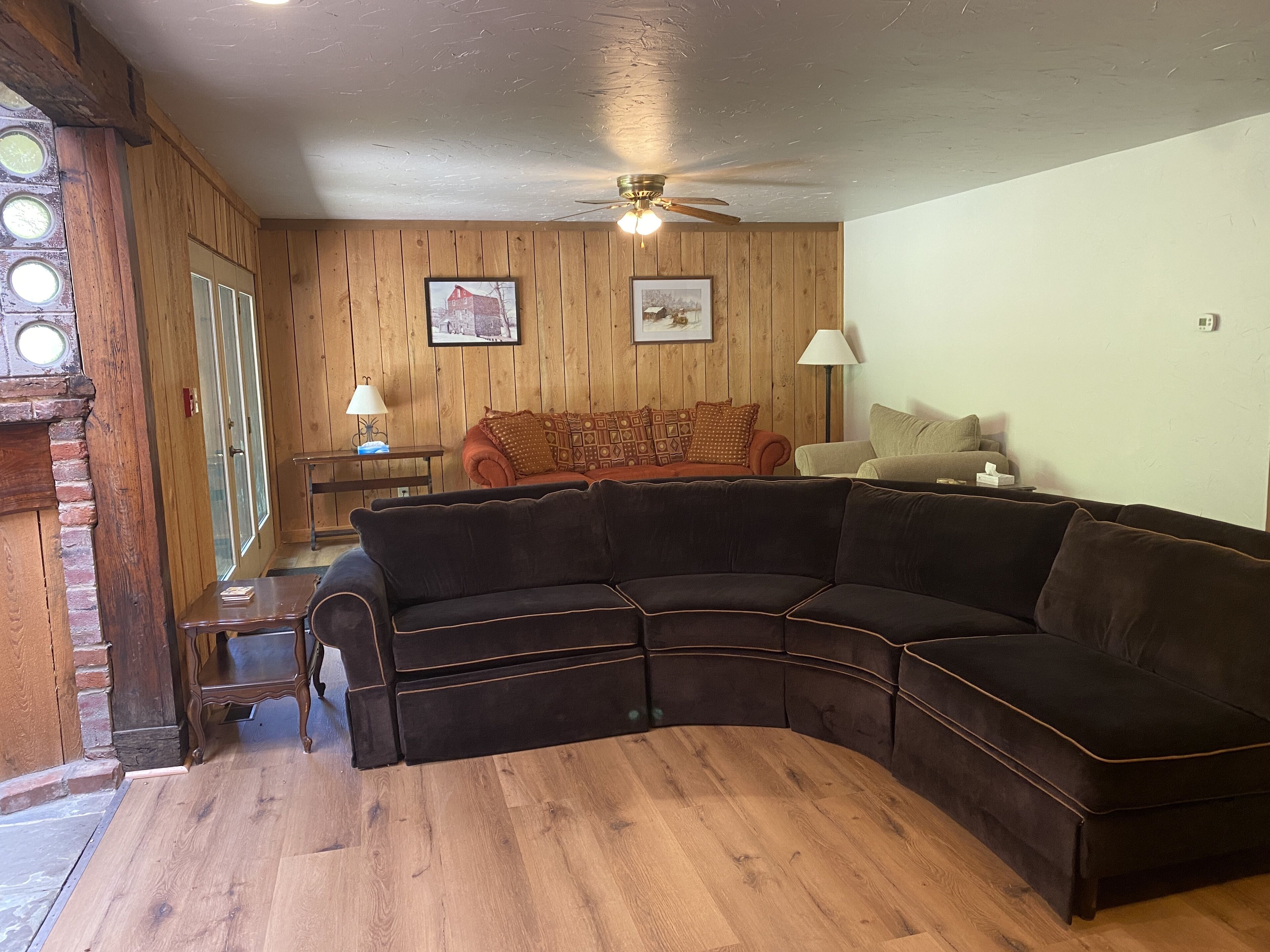Ein gemütliches Wohnzimmer mit einer gebogenen Eckcouch, Holzboden und Deckenventilator.