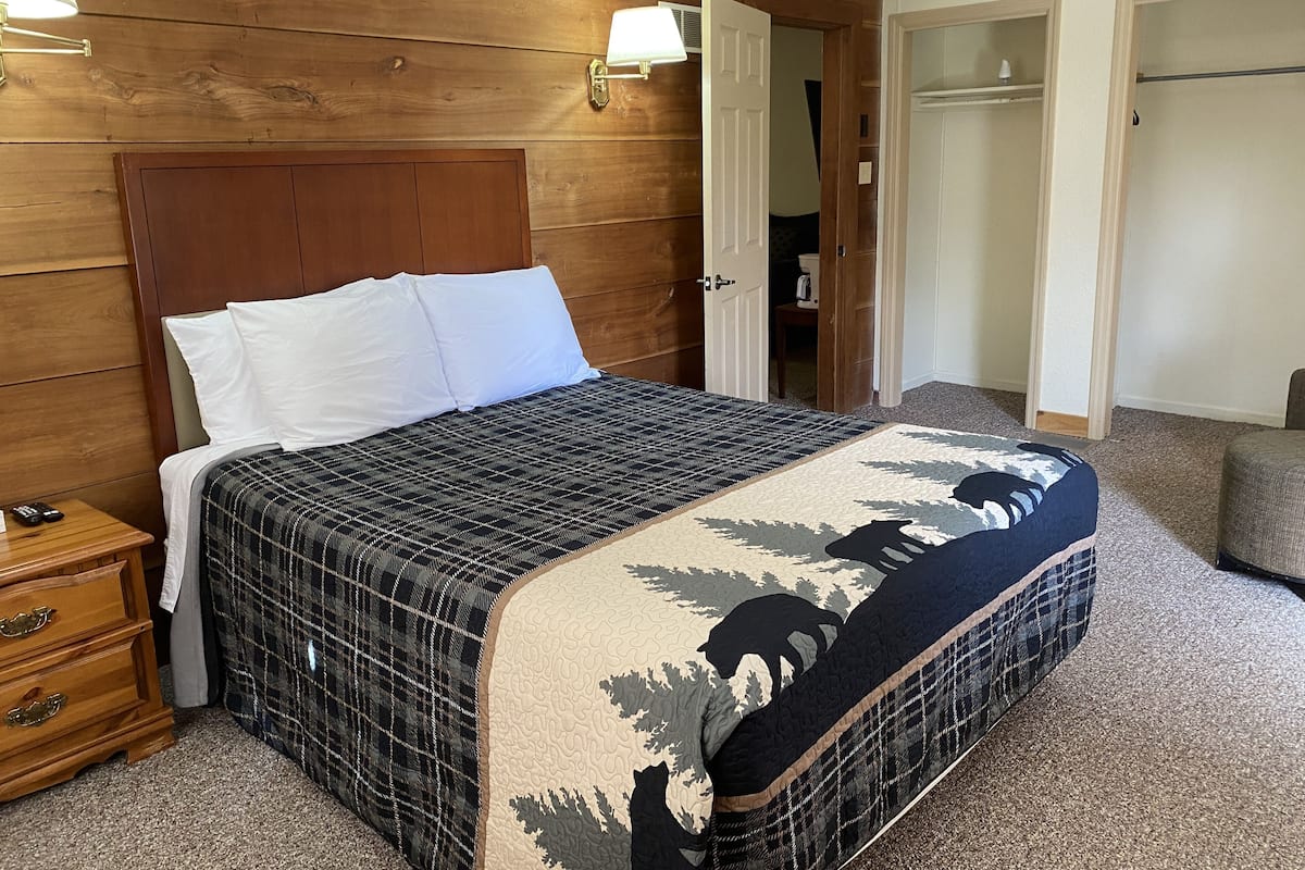 Un lit bien fait, recouvert d’une couverture à carreaux, avec une tête de lit en bois et deux lampes de chevet.