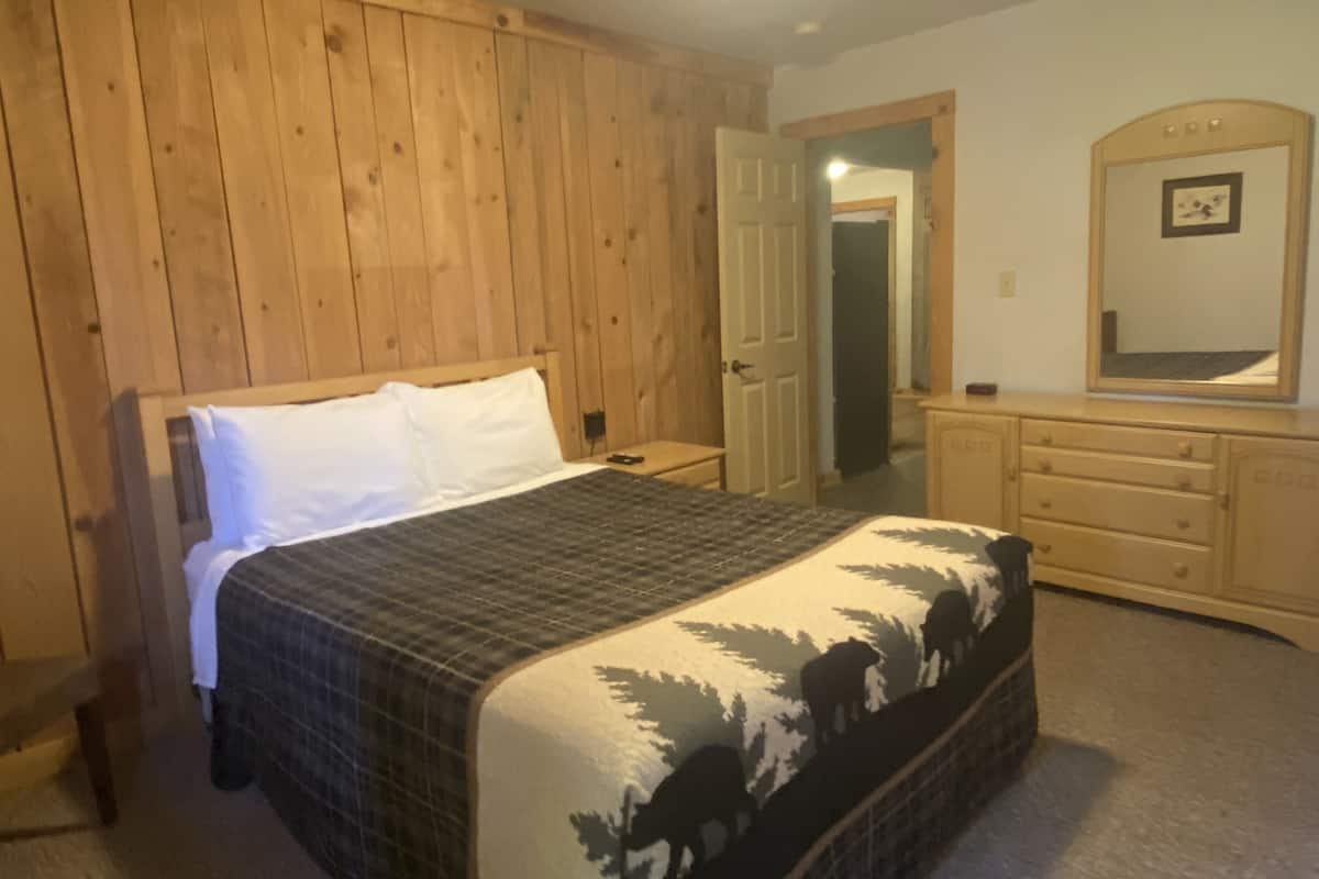 Une chambre à coucher avec une tête de lit en bois, un lit recouvert d’une couvre-lit à motifs, une commode et un miroir.