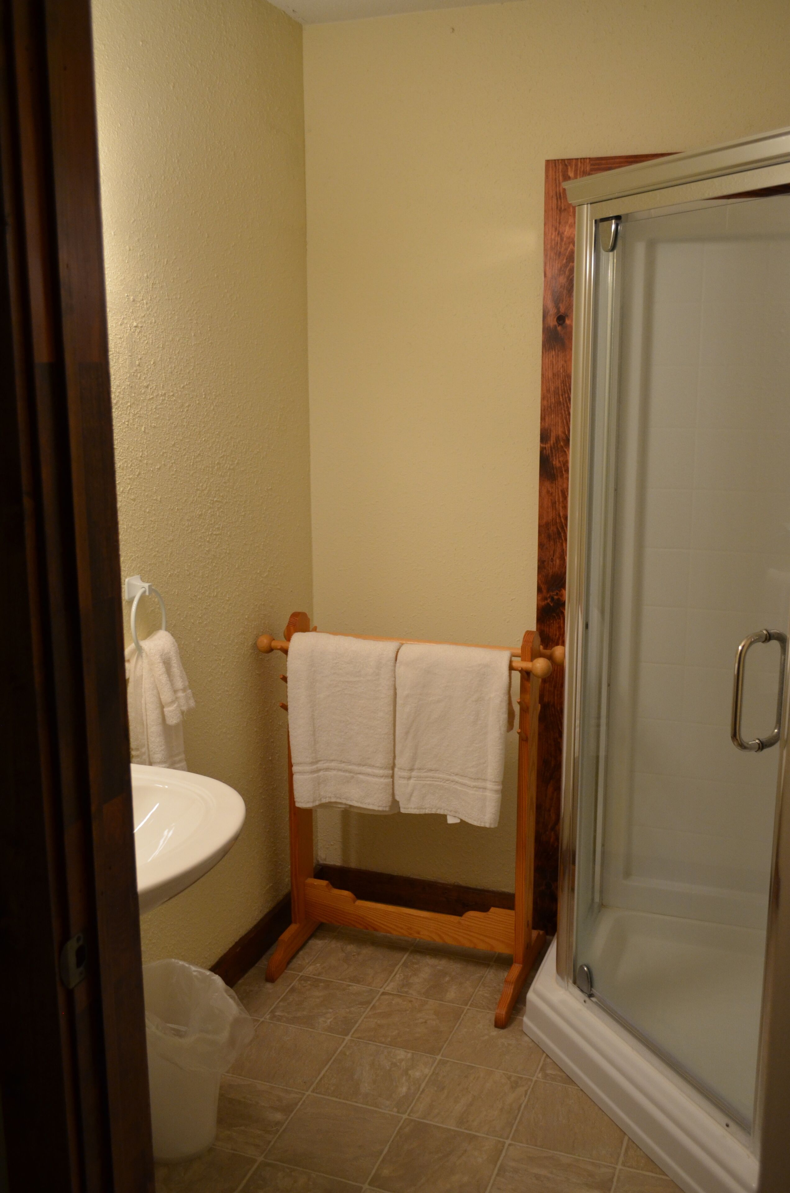 Un baño con un perchero de madera, un lavamanos blanco y una cabina de ducha de vidrio.