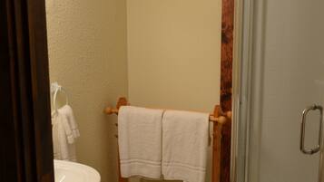 Un baño con un perchero de madera, un lavamanos blanco y una cabina de ducha de vidrio.
