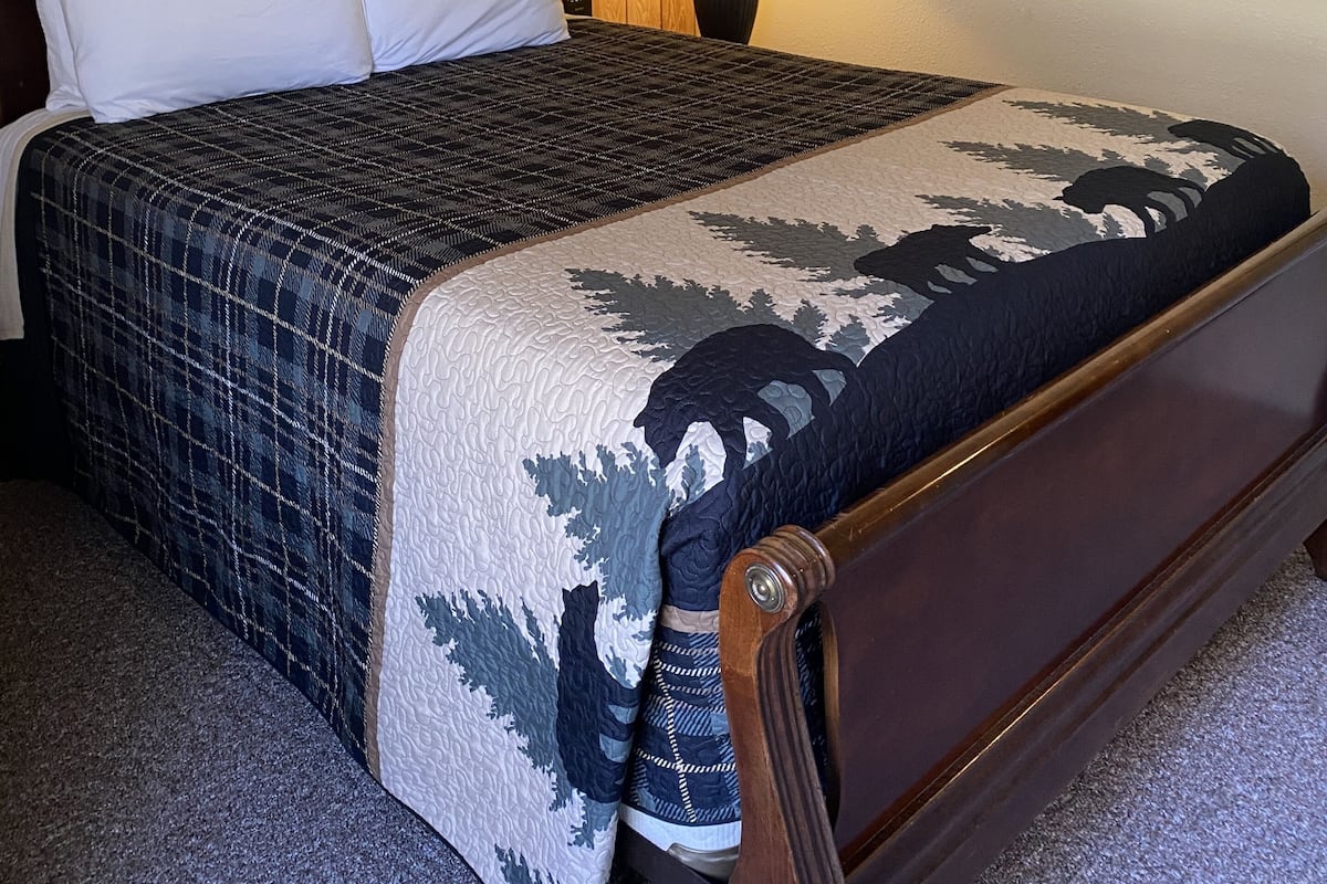 Un lit bien fait, avec une couvre-lit à motifs, une tête de lit en bois, une lampe de chevet et un tableau encadré accroché au mur.