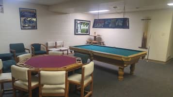 A pool table with chairs around it, a billiards table, and framed advertisements on the wall.