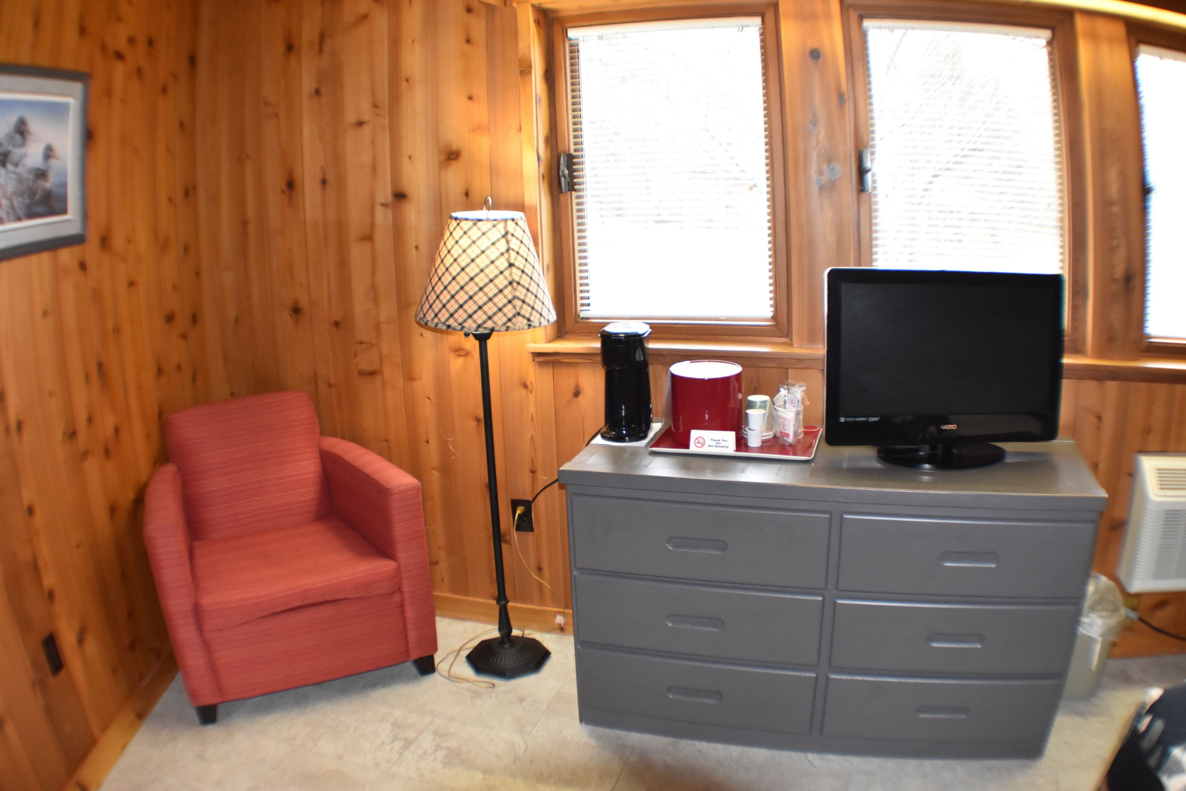 A room with a red chair, a grey dresser, a television, and a lamp.