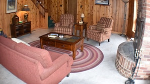 Ein gemütliches Wohnzimmer mit Kamin, Holzwänden, einem roten Sofa und gemusterten Sesseln.
