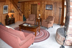 Una sala de estar acogedora con chimenea, paredes de madera, un sofá rojo y sillones estampados.