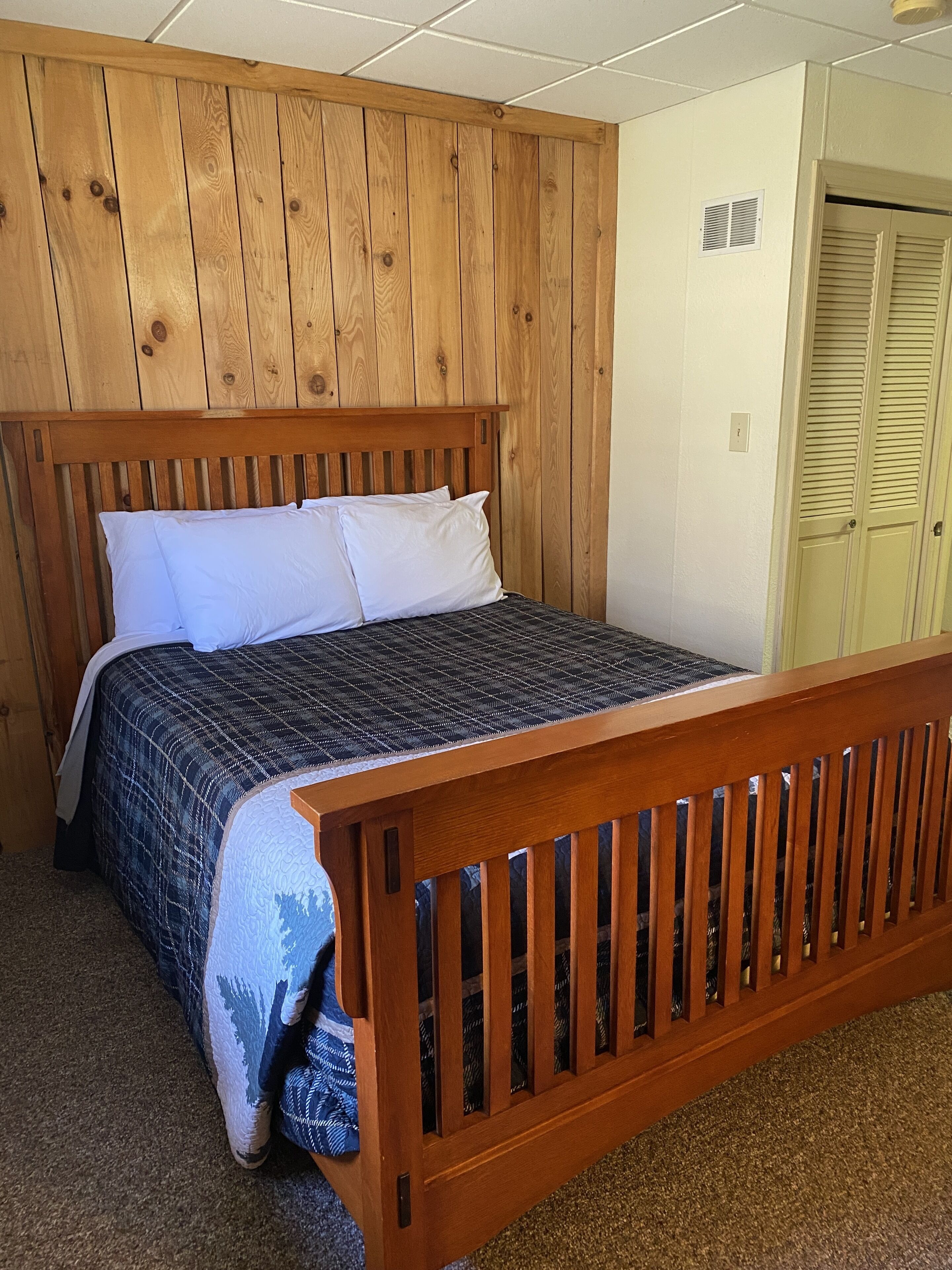 A bedroom with a wooden headboard, a bed with a plaid bedspread, and a wooden bench at the foot of the bed.