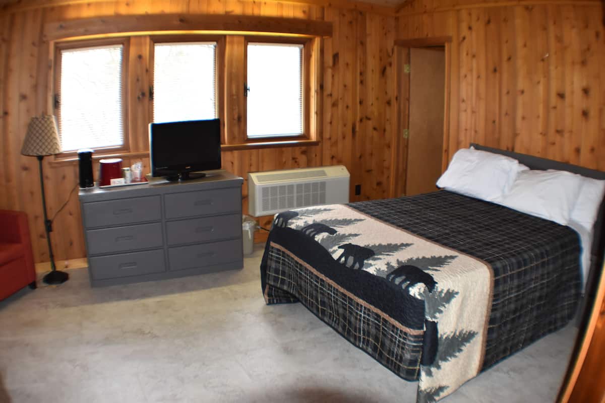 Une chambre à coucher avec un lit, une commode, une télévision et des fenêtres.