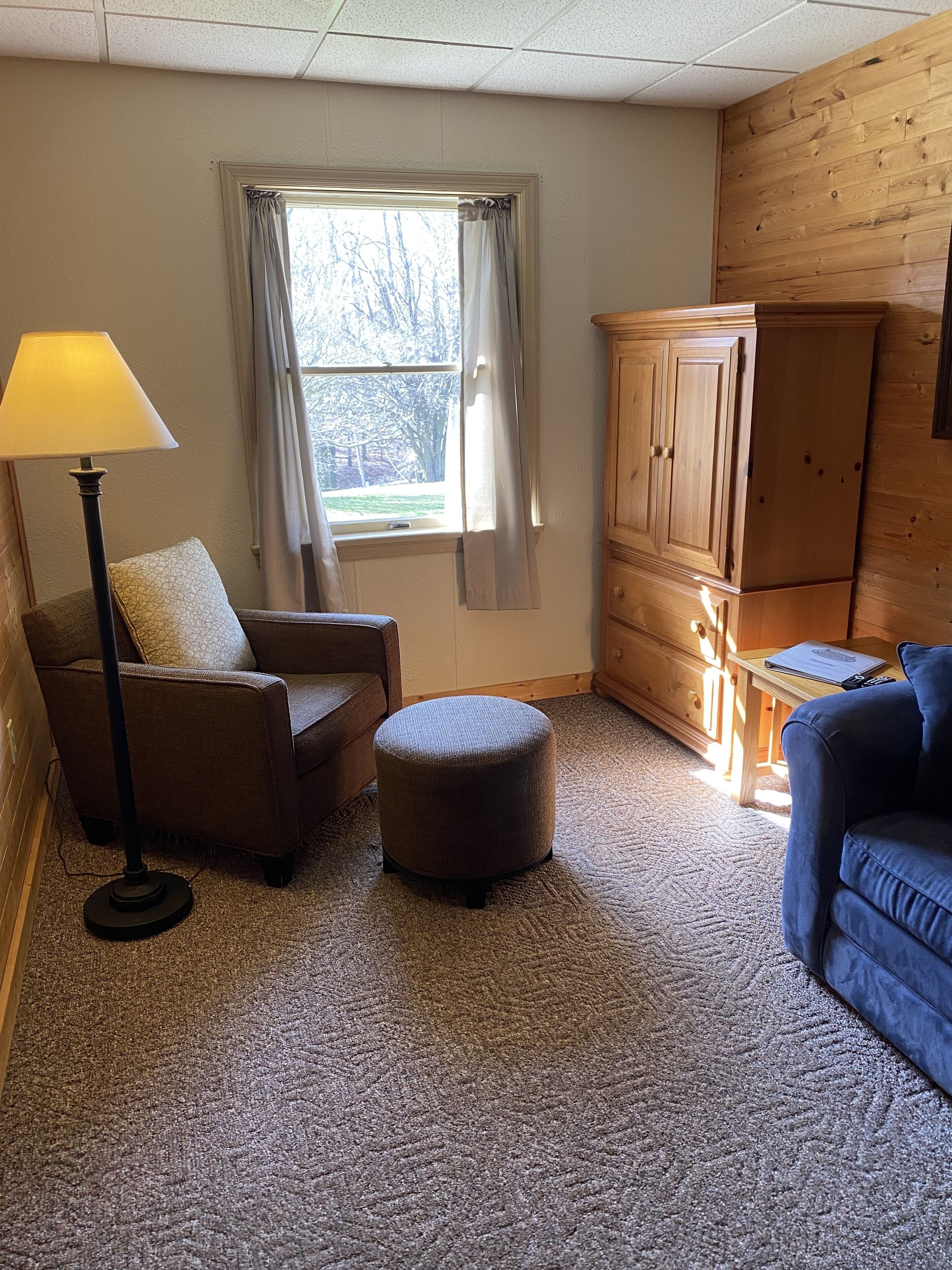 A living room with a sofa, ottoman, floor lamp, and wooden cabinet.