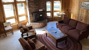 Ein gemütliches Wohnzimmer mit Kamin, Holzwänden, großen Fenstern und bequemen Sitzmöglichkeiten.