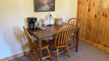 Una mesa de comedor de madera con cuatro sillas, una cafetera, una lámpara y un cuadro en la pared.