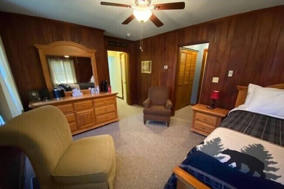 Une chambre à coucher comprenant un lit, une commode, une chaise, une table de chevet et un ventilateur de plafond.