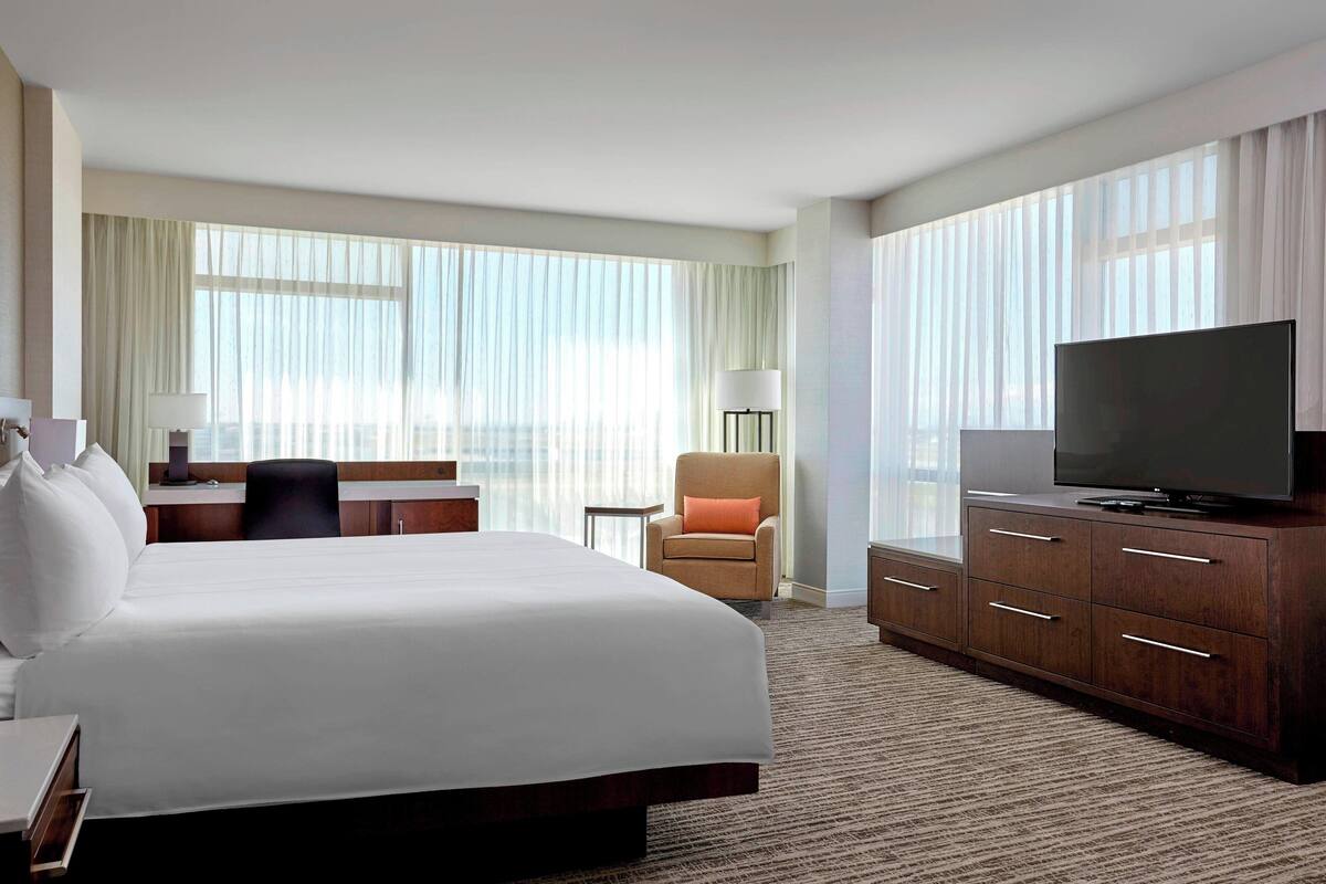 A hotel room with a large bed, a desk with a chair, a television, and a window with curtains.