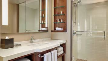 A modern bathroom with dual sinks, a large mirror, glass shelves with toiletries, and a walk-in shower.
