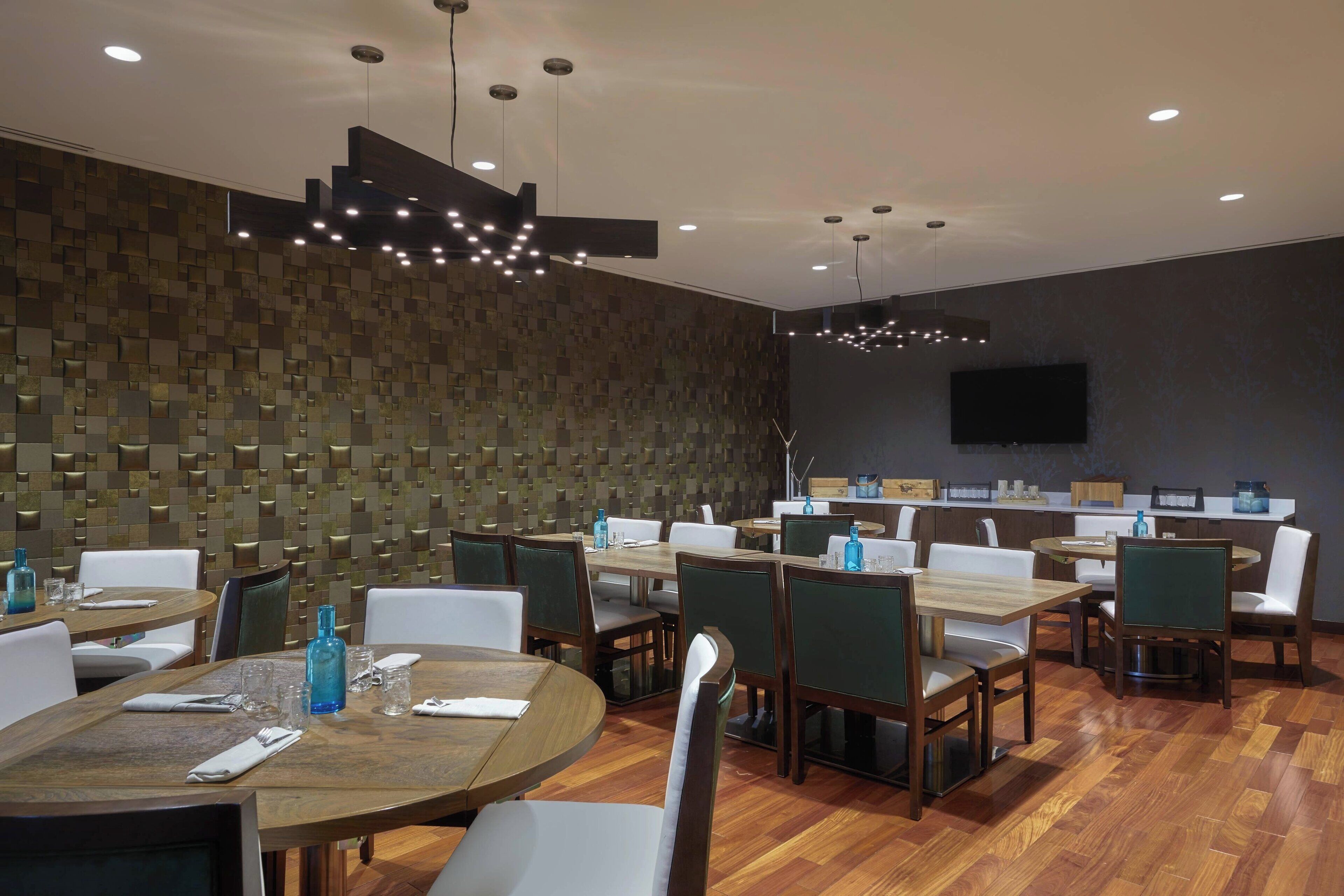 A modern dining area with wooden tables and chairs, a patterned wall, and recessed lighting.