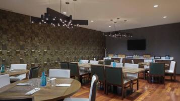 A modern dining area with wooden tables and chairs, a patterned wall, and recessed lighting.
