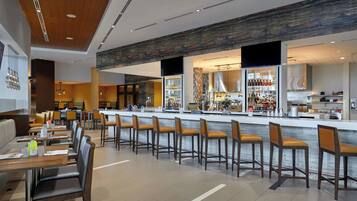 A modern bar area with a long counter, multiple seating options, and a visible kitchen in the background.