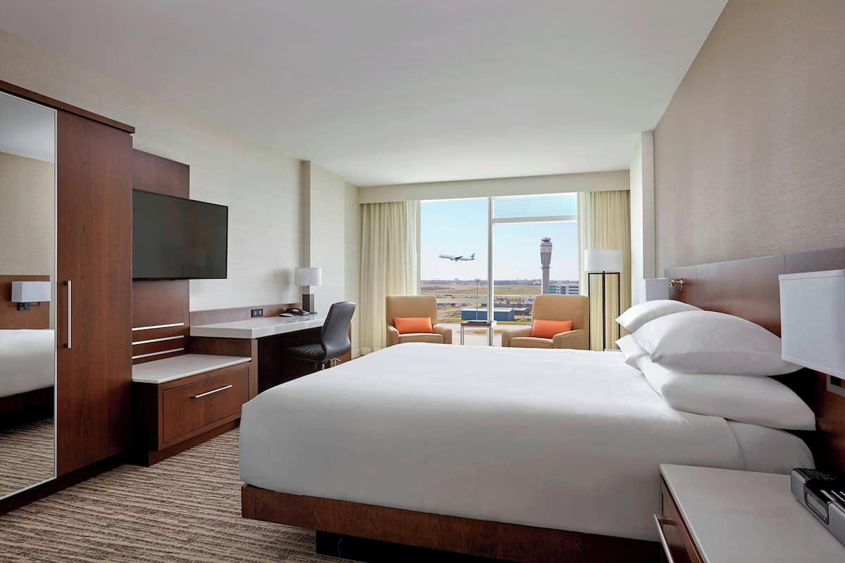 A hotel room with a large bed, a desk, a TV, and a view of an airport.