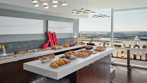 A breakfast buffet with pastries, fruits, and beverages, set against a backdrop of a large window overlooking an airport. - Calgary Airport Marriott In-Terminal Hotel (Calgary)