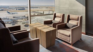 A modern airport lounge with comfortable seating and a large window offering a view of the airport tarmac and city skyline.
