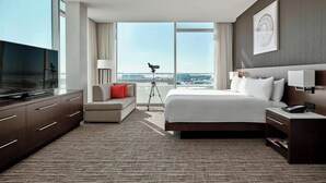 A modern hotel room with a large bed, a TV, a sofa, and a view of the cityscape.
