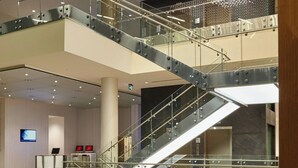 A modern hotel lobby with a central staircase, a reception desk, and a seating area with a table and chairs.