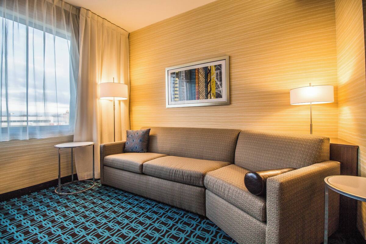 A hotel room with a sofa, two side tables, a framed picture on the wall, and a patterned carpet.