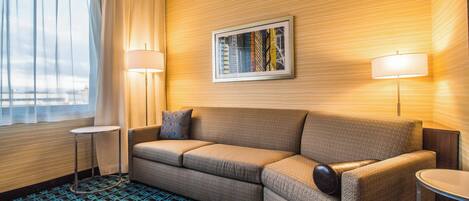 A hotel room with a sofa, two side tables, a framed picture on the wall, and a patterned carpet.