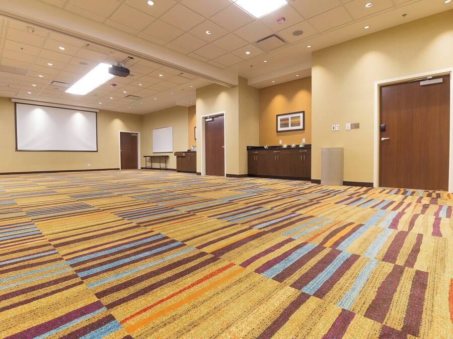 Un amplio salón de conferencias con alfombra estampada, una pantalla de proyector, una pizarra y un mostrador de recepción.
