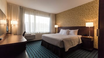 A hotel room with a bed, bedside tables, a desk, and a large window with curtains.