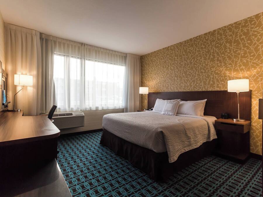 A hotel room with a bed, bedside tables, a desk, and a large window with curtains.