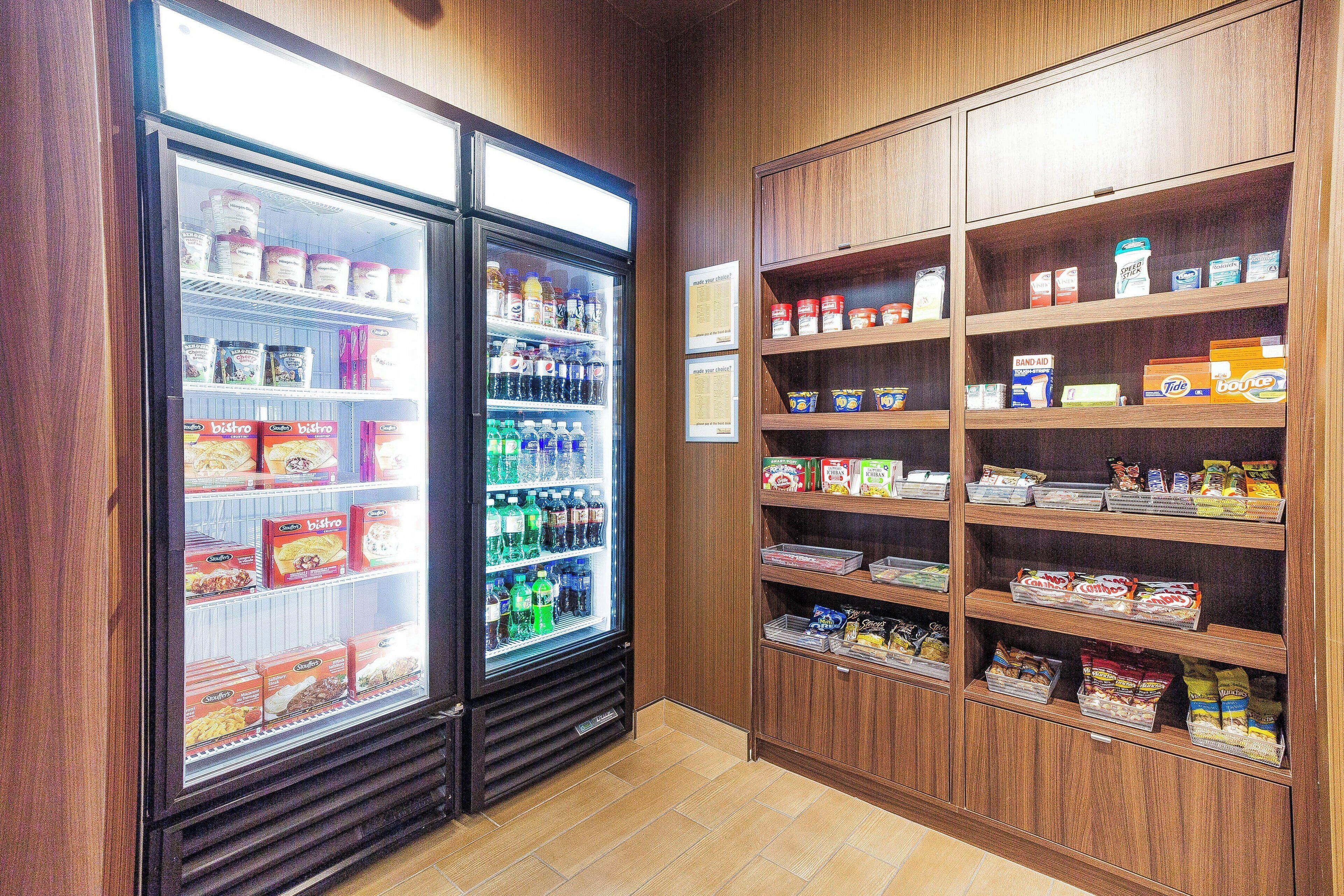 Un refrigerador exhibe diversos alimentos y un estante repleto de aperitivos y bebidas.