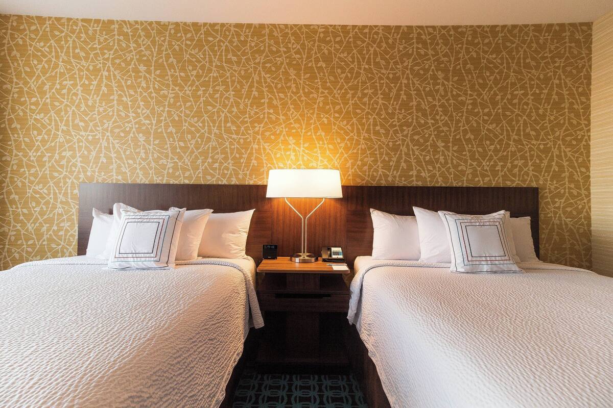 A hotel room with two beds, a nightstand with a lamp, and patterned wallpaper.
