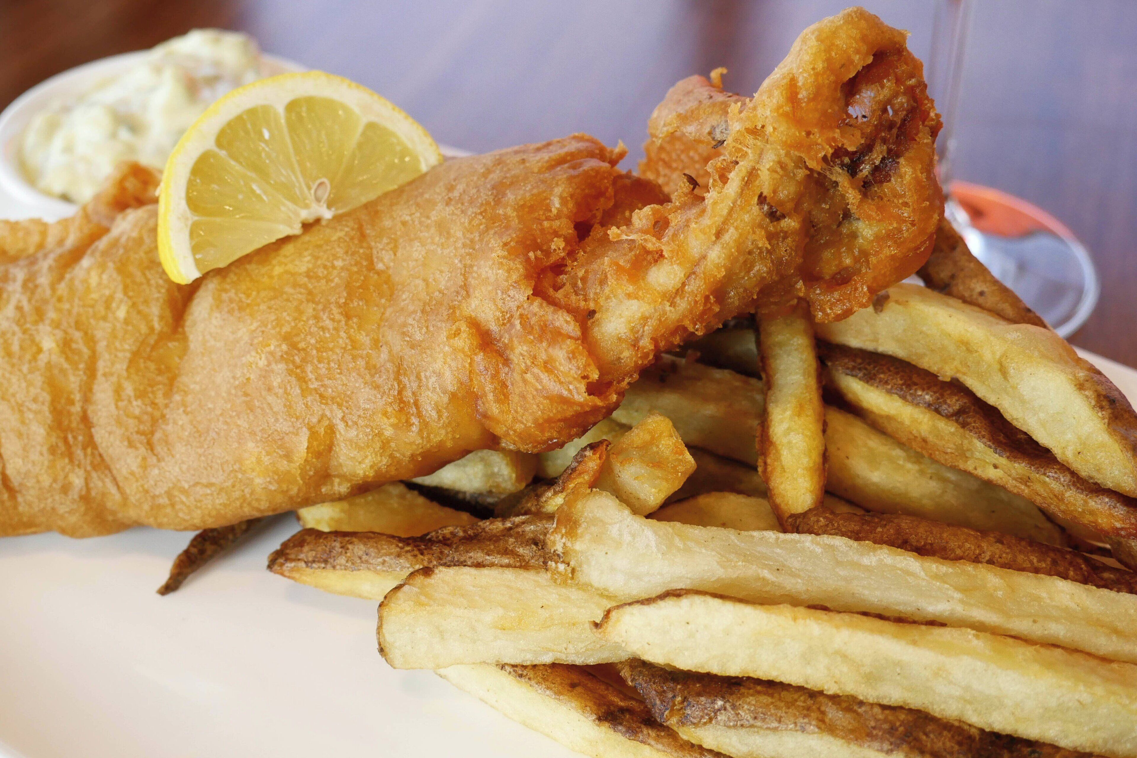 A plate of fish and chips with a lemon wedge and a small bowl of tartar sauce.