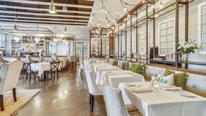 Un restaurant spacieux avec de nombreuses tables, des nappes blanches et un bar situé au fond de la salle.